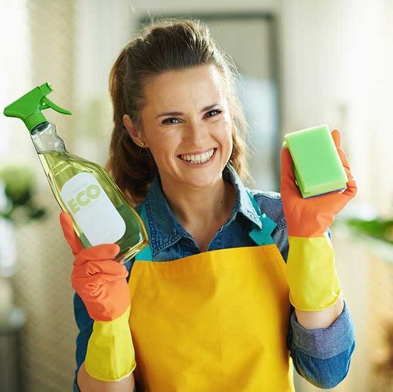 Lächelnde moderne Frau mit Reinigungsmittel und Schwamm
